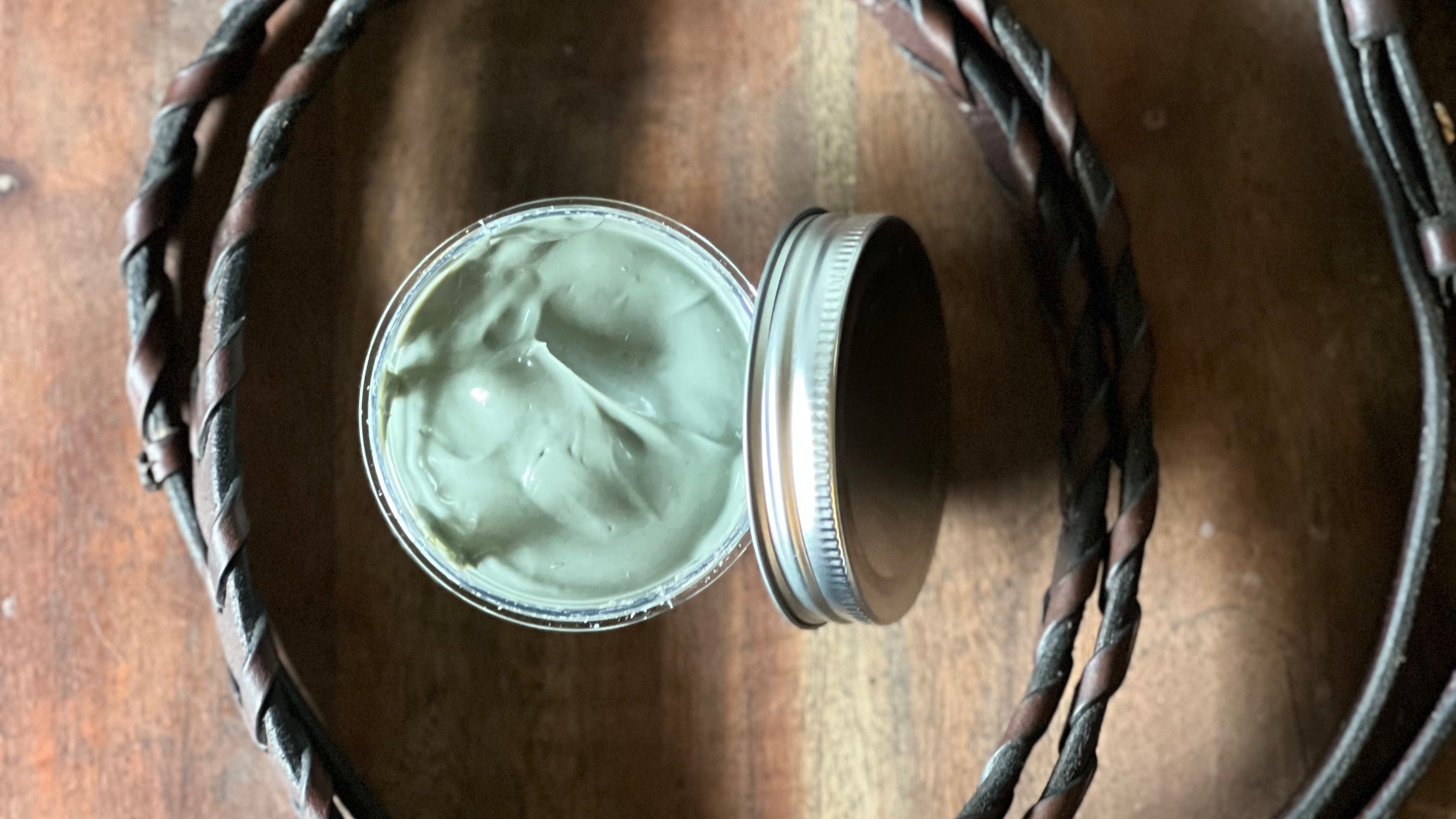 Greenish cream in jar with tin lid on wooden table