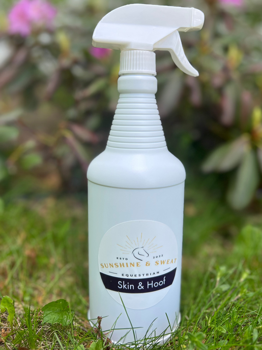 White spray bottle labeled 'Sunshine & Sweat' on grass with blurred flowers in the background